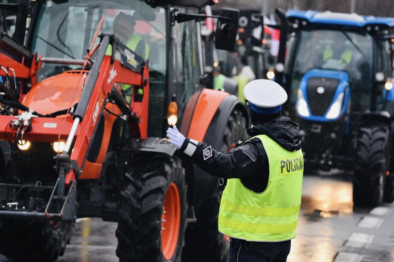 Zdjęcie przedstawia ciągniki i policjanta kierującego ruchem. - grafika rozmowy