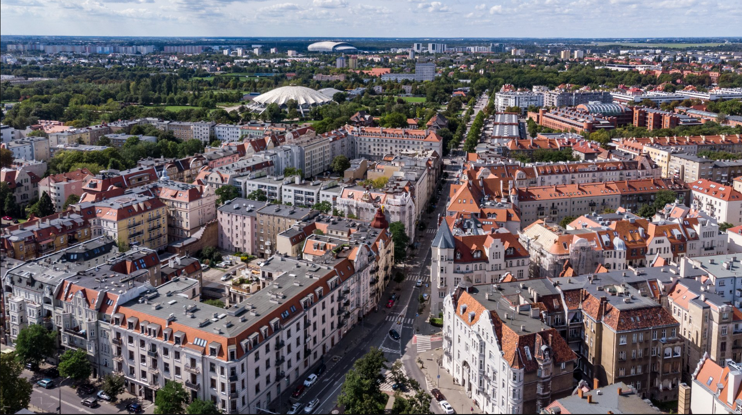 Na zdjęciu panorama Poznania z lotu ptaka, widać kamienice, w tle Arenę - grafika rozmowy