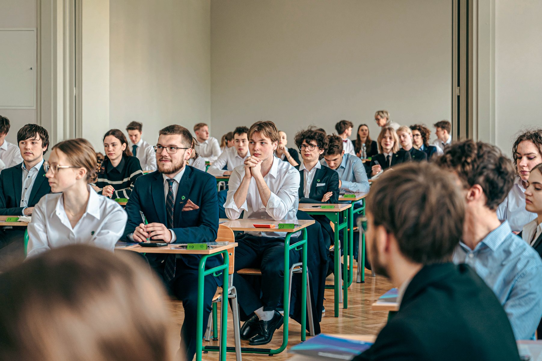 Zdjęcie przedstawia maturzystów siedzących w ławkach. - grafika rozmowy