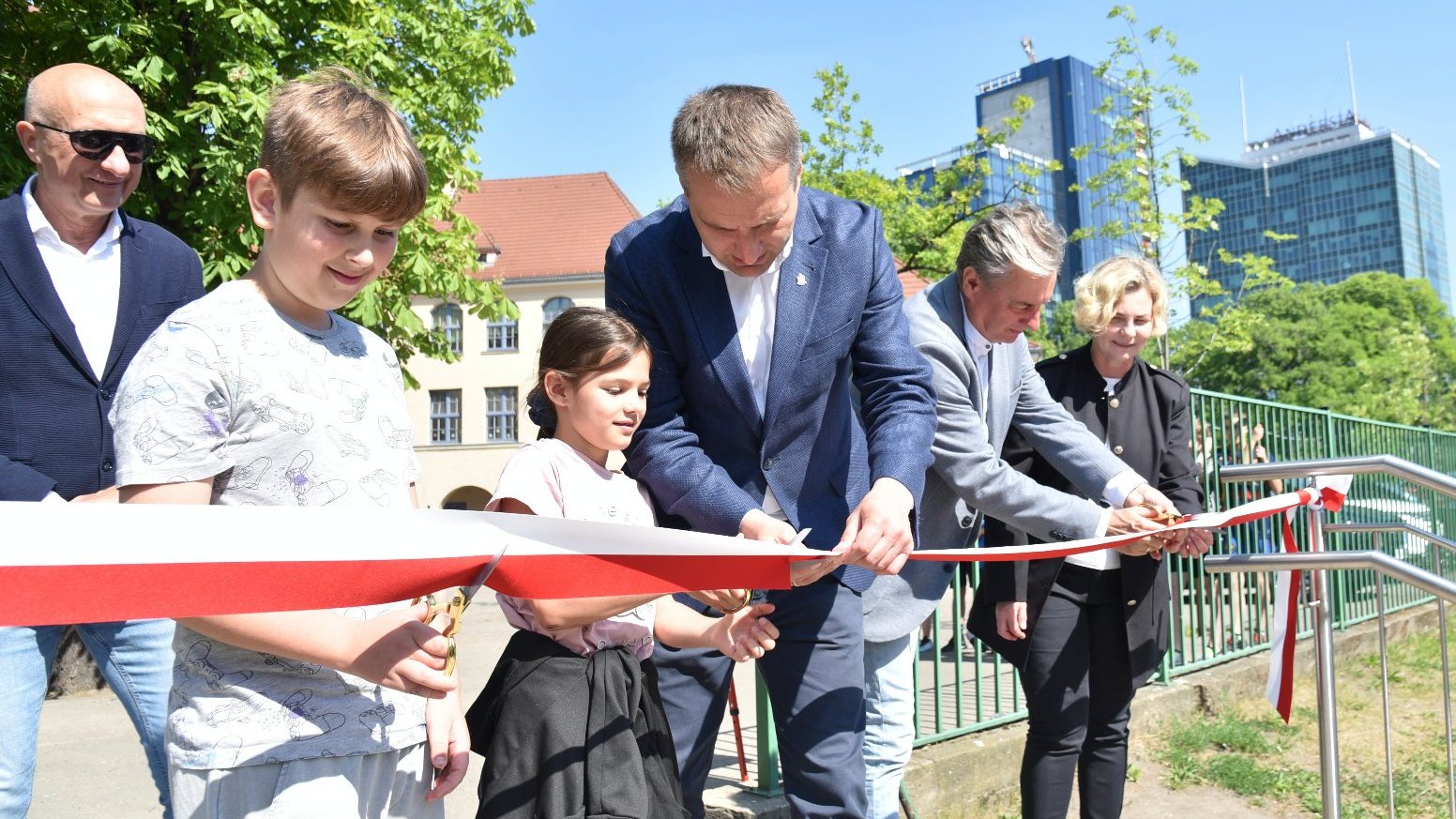 Zdjęcie przedstawia dorosłych i dziecio podczas przecinania wstęgi.