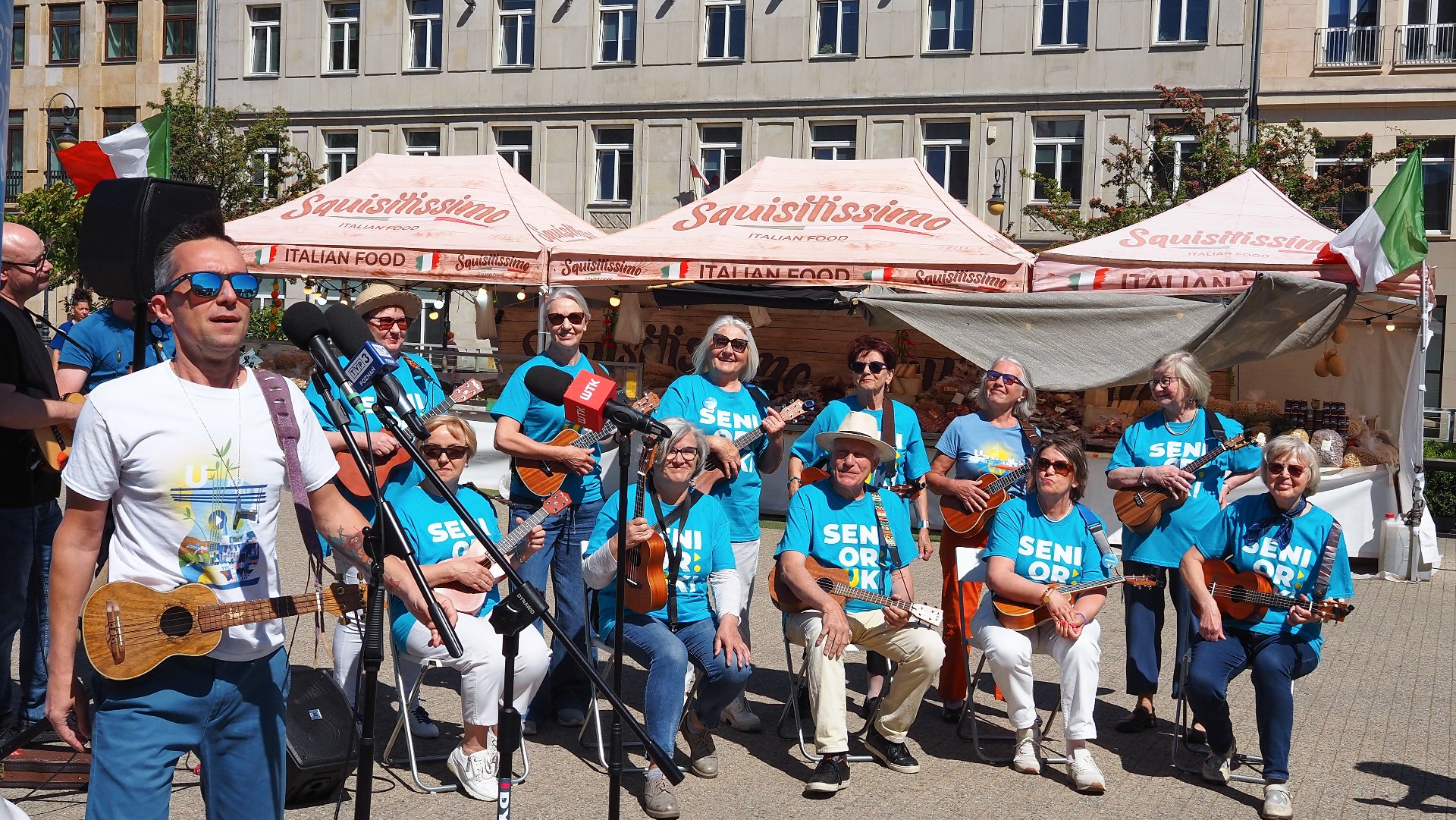 Na zdjęciu zespół seniorów w niebieskich koszulkach, każdy ma ukulele w ręku - grafika rozmowy