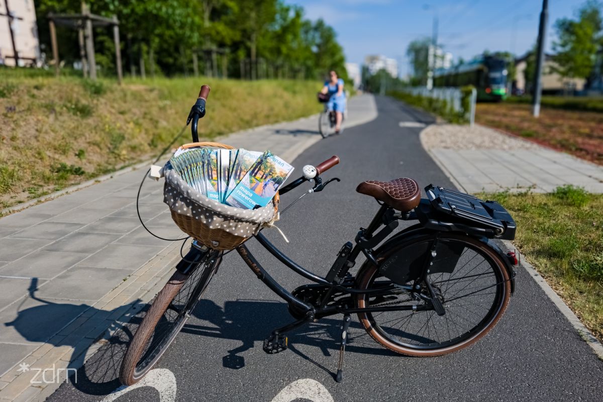 Stojący rower, w którym przednim bagażniku włożone są mapy rowerowe - grafika rozmowy