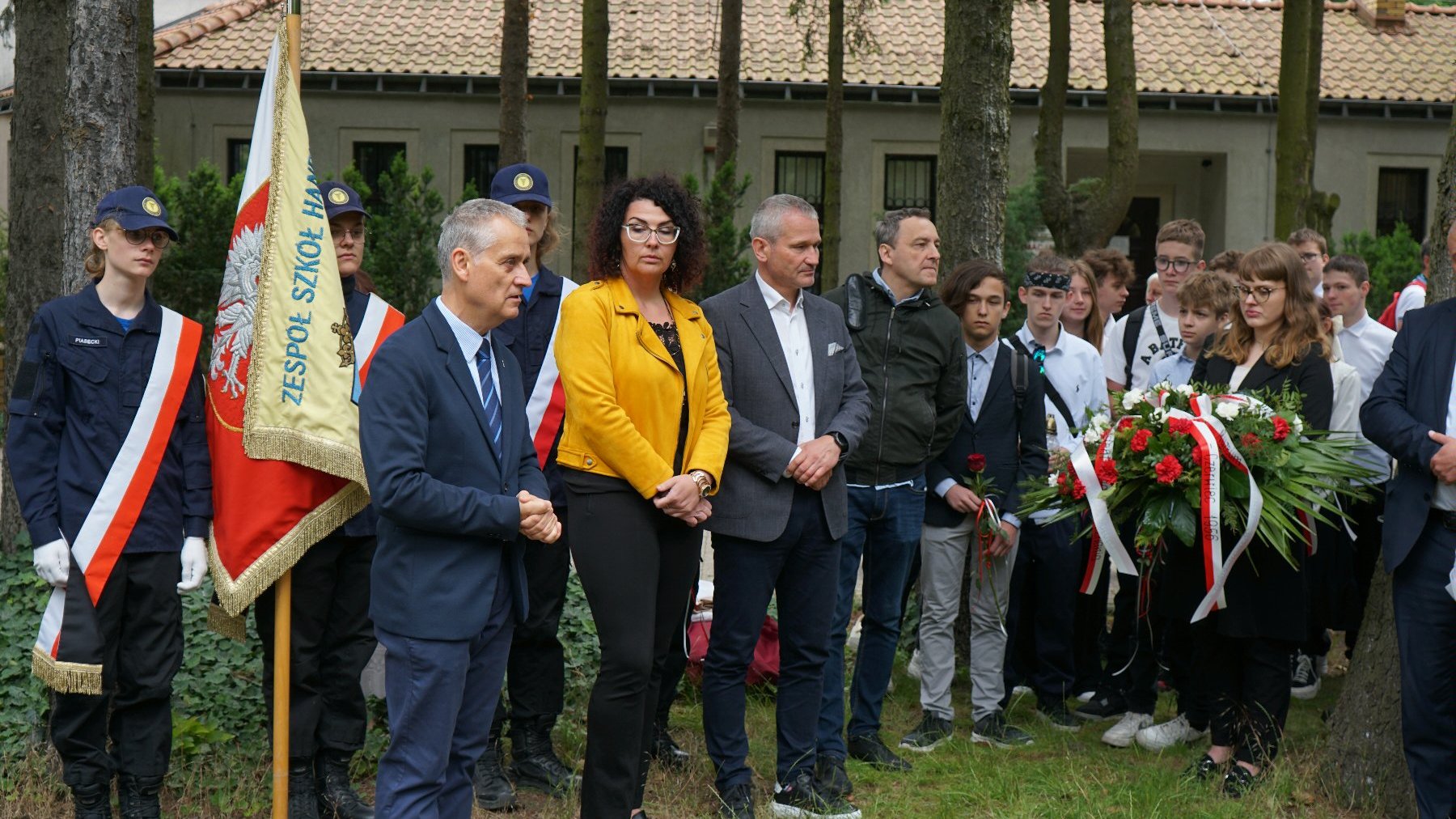 Zdjęcie przedstawia młodziedż i dorosłych na cmentarzu.