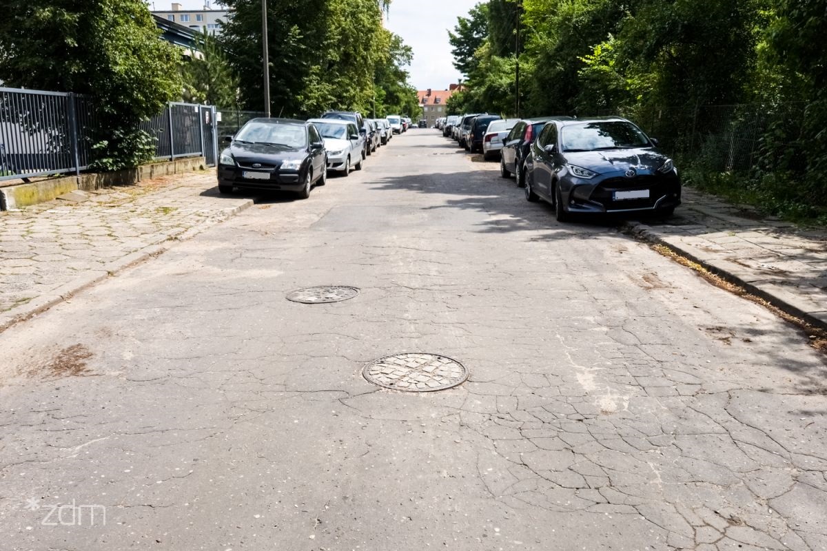 Zdjęcie przedstawia ulicę. Po jej obu stronach stoją zaparkowane samochody. - grafika rozmowy