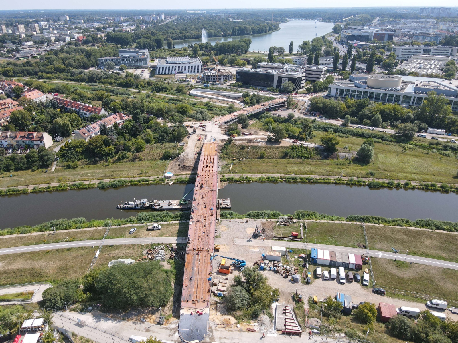 Zdjęcie przedstawia budowane mosty nad rzeką i otaczające budynki widziane z lotu ptaka. - grafika rozmowy