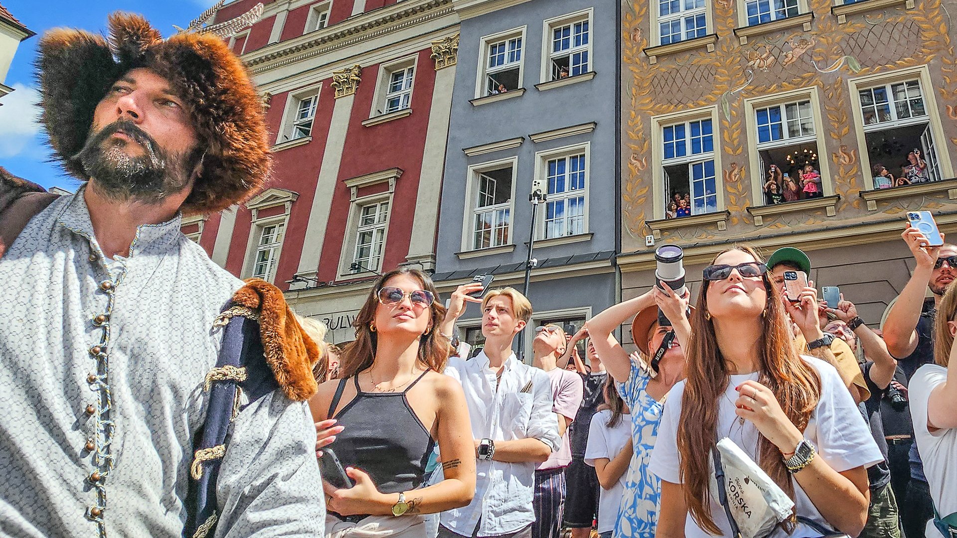 Na zdjęciu grupa młodych ludzi na Starym Rynku, obok mężczyzna w historycznym stroju - grafika rozmowy