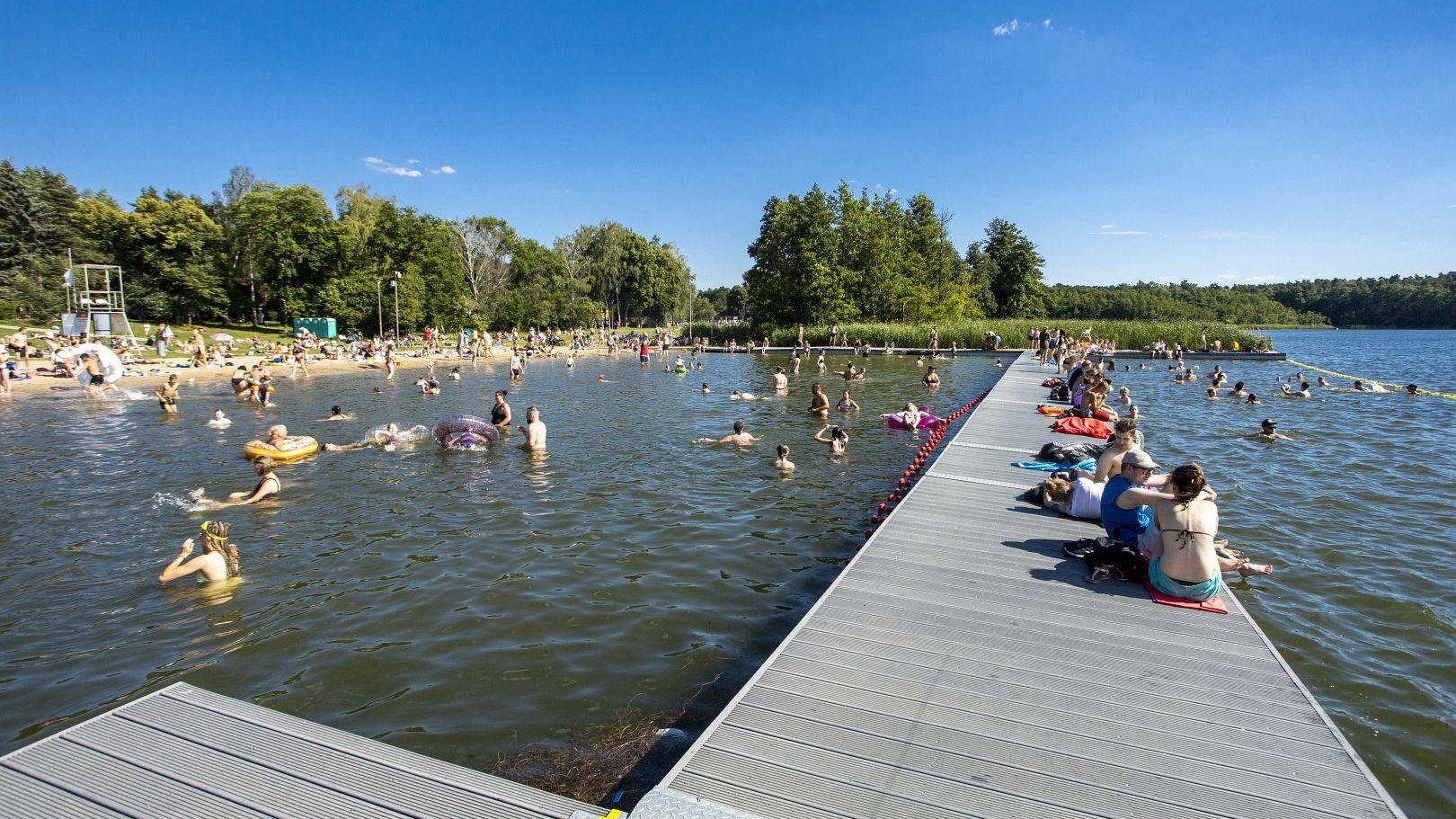 Zdjęcie przedstawia ludzi w wodzie, na pomoście i na plaży. - grafika rozmowy