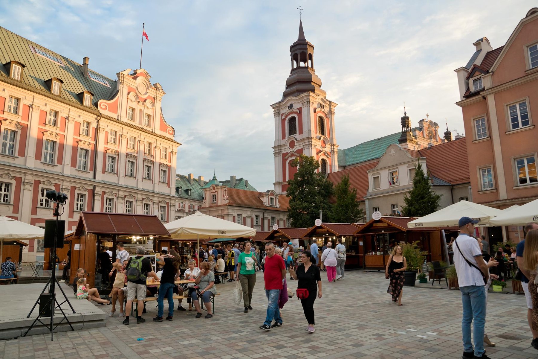 Zdjęcie przedstawia plac Kolegiacki, na kórym stoją stragany i spacerują ludzie. - grafika rozmowy