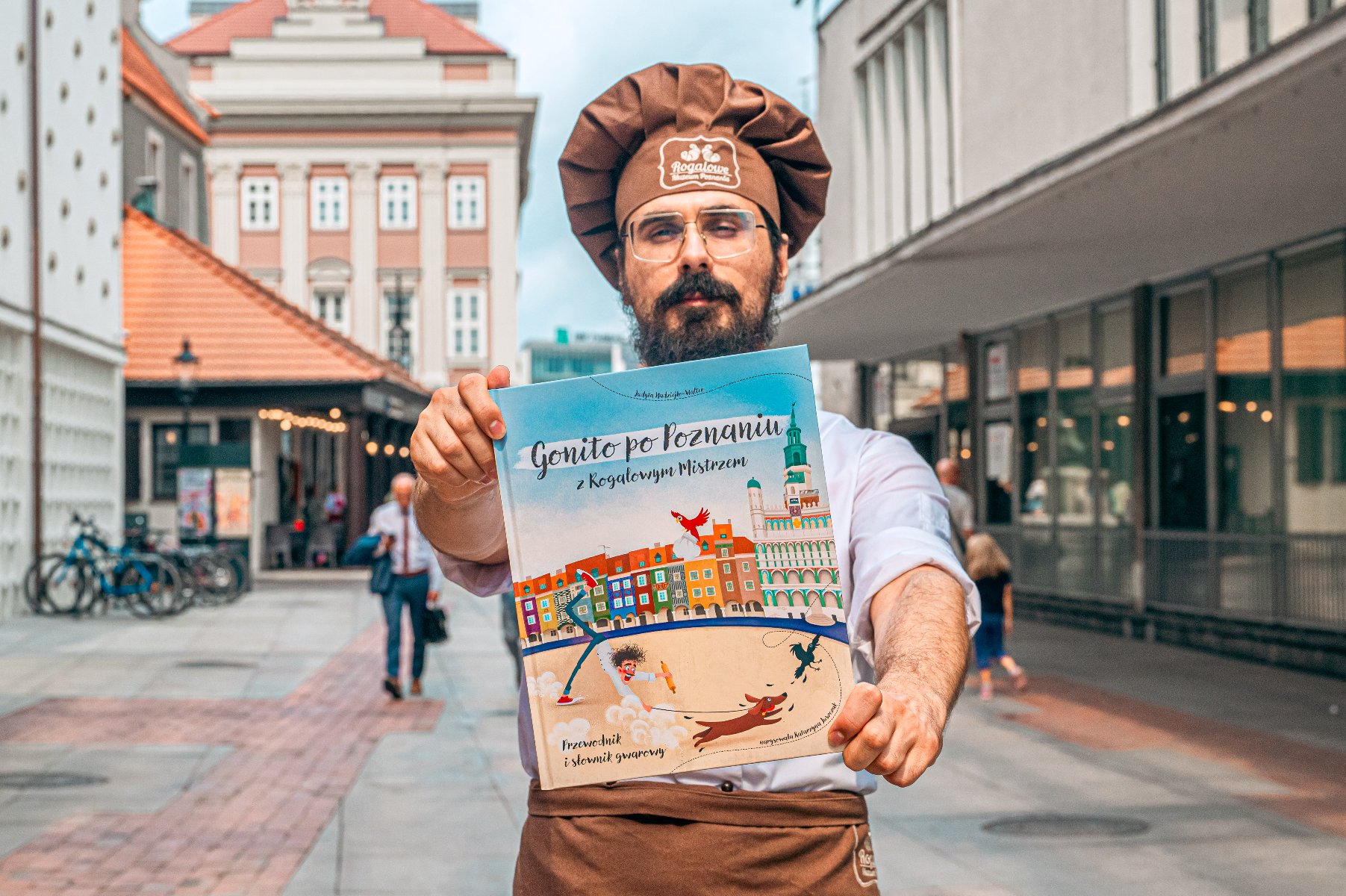 Na zdjęciu mężczyzna w czapce cukiernika trzymający książkę - grafika rozmowy