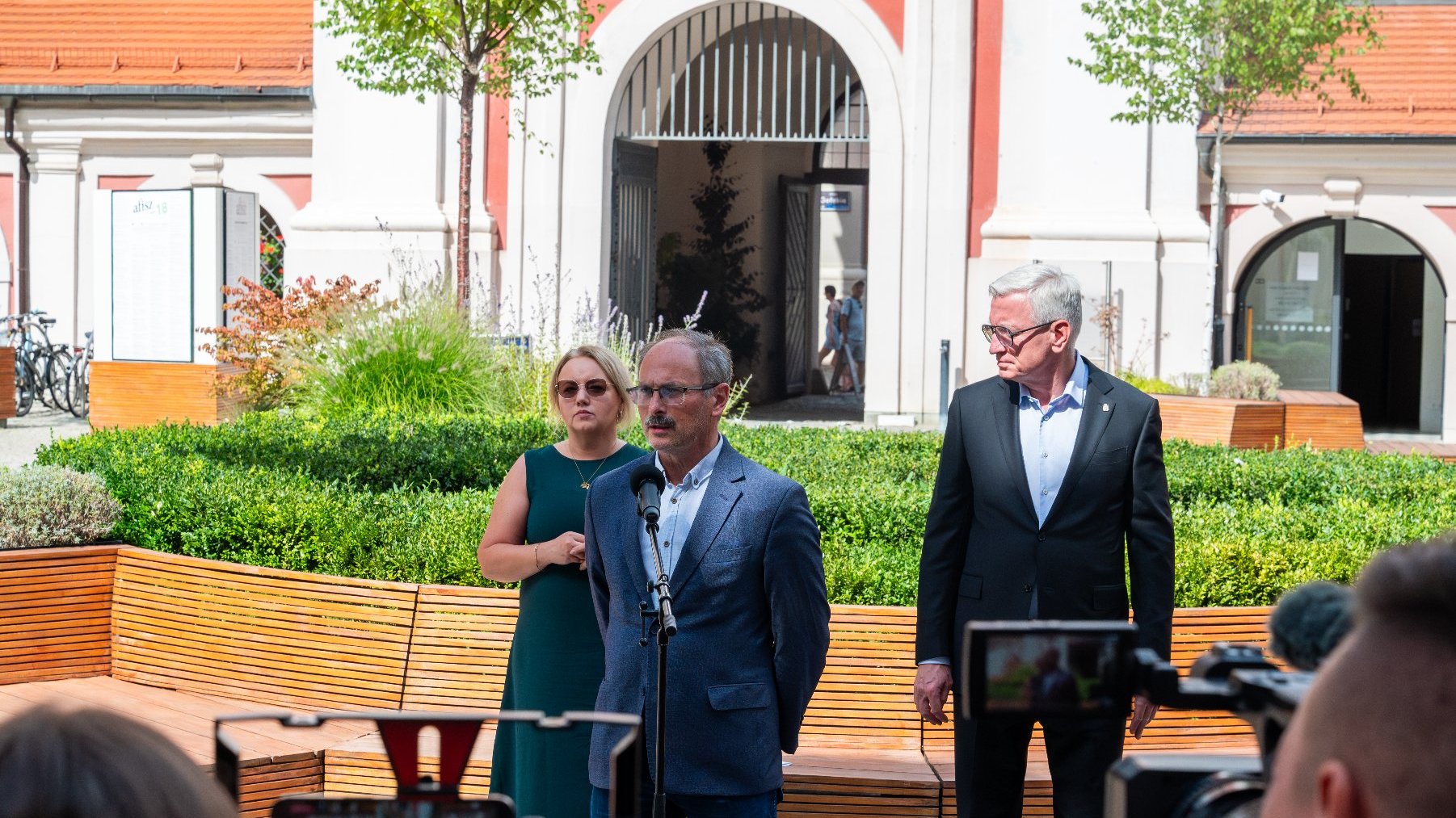 Na zdjęciu trzy osoby podczas briefingu prasowego, na pierwszym planie mężczyzna, za nim meżczyzna i kobieta