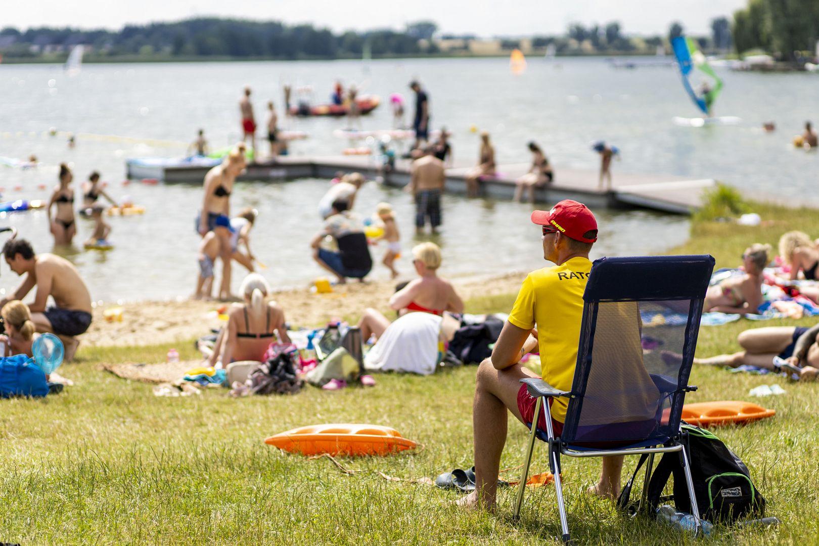 Zdjęcie przedstawia ratownika na plaży. W tle widać ludzi w wodzie. - grafika rozmowy