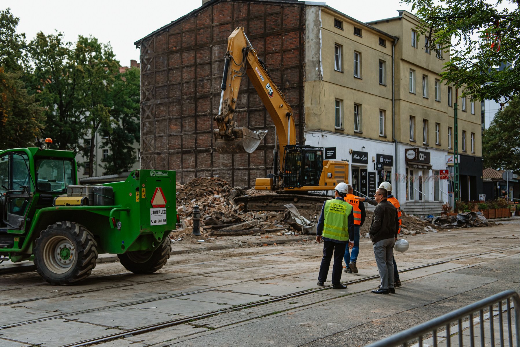 Na zdjęciu czterej mężczyźni przyglądający się rozbiórce kamienicy - grafika rozmowy