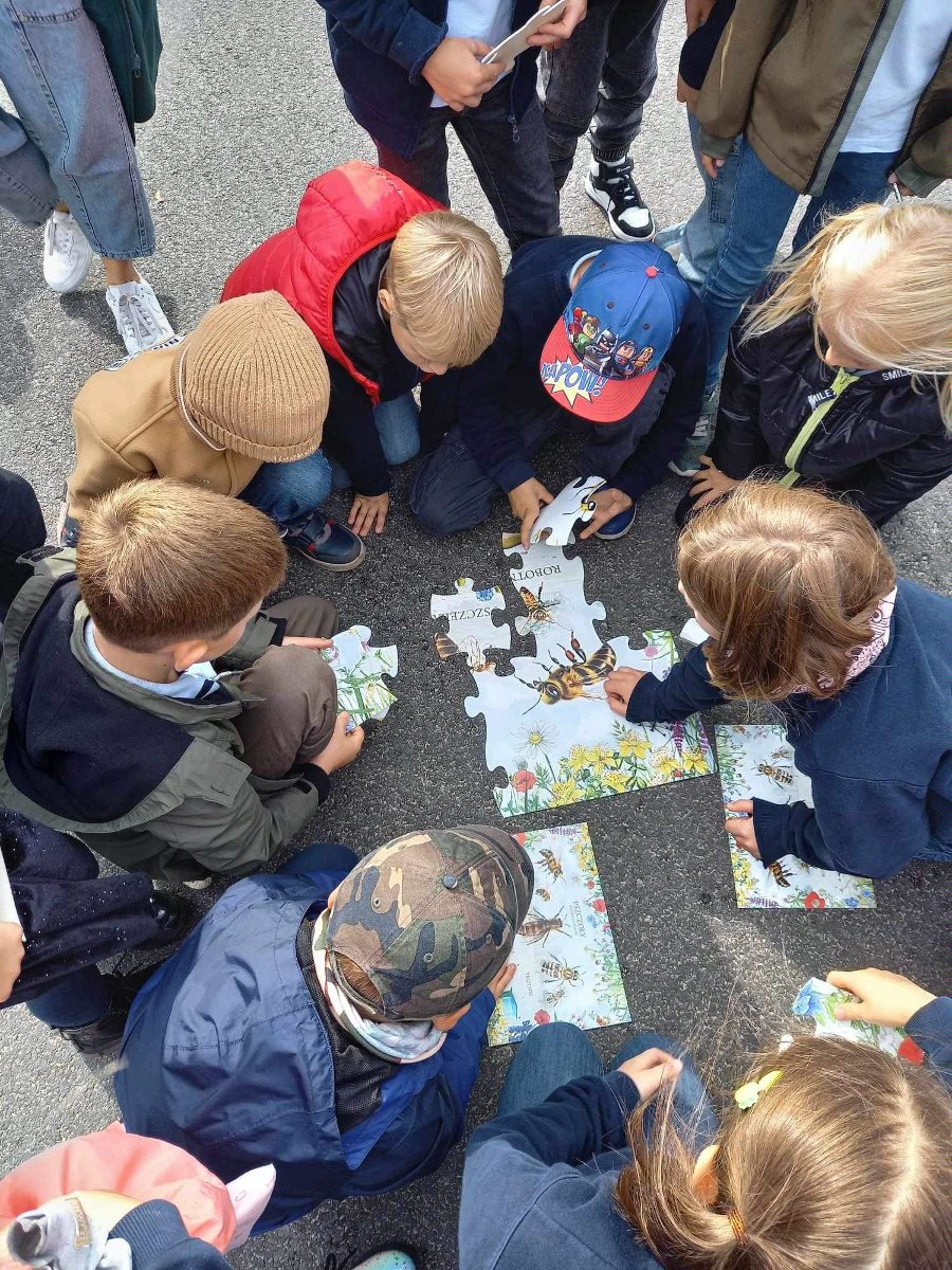 Zdjęcie przedstawia dzieci siedzace w okręgu i układające puzzle. - grafika rozmowy