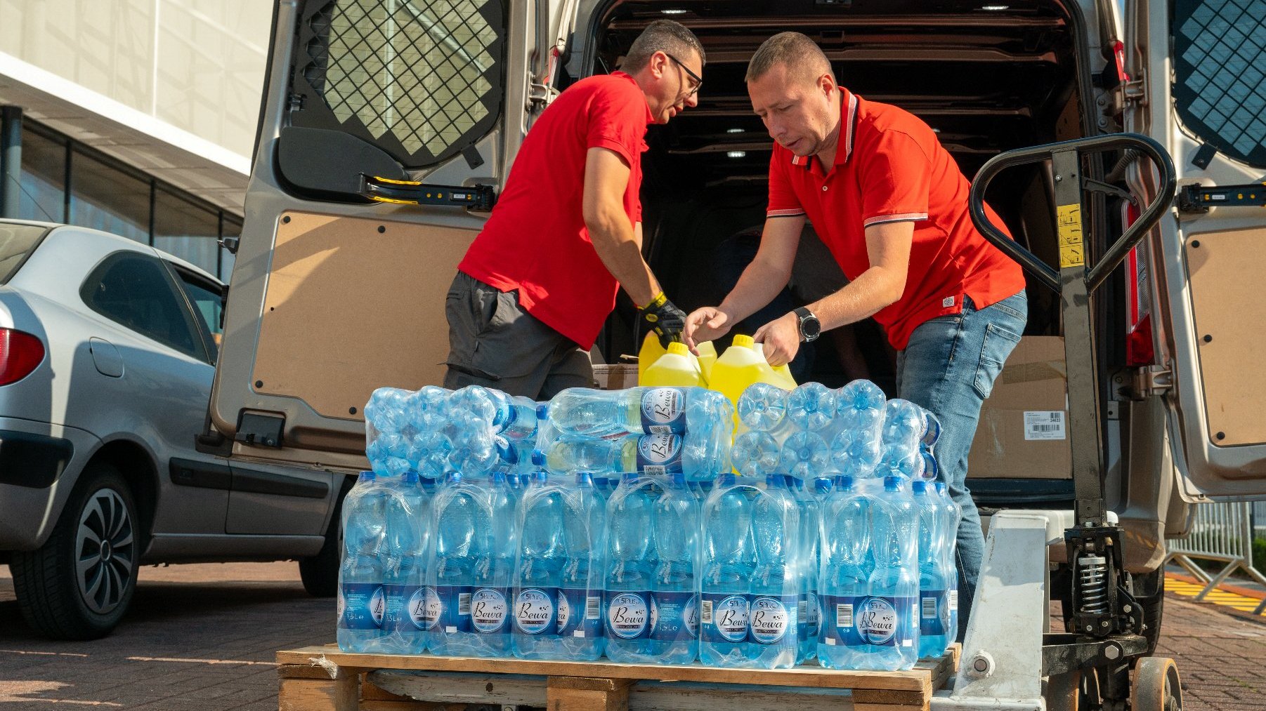 Na zdjęciu dwóch mężczyzn ładuje butelkowaną wodę do samochodu