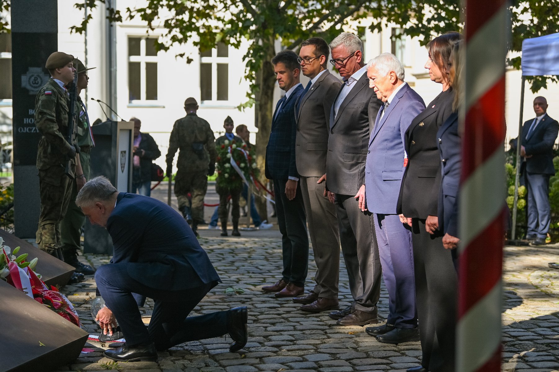 Zdjęcie przedstawia ludzi podczas składania kwiatów. - grafika rozmowy