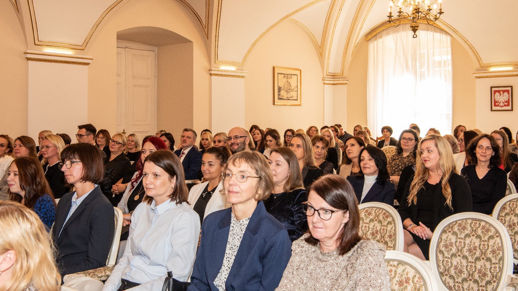 Zdjęcie przedstawia tłum ludzi siedzących na krzesłach.