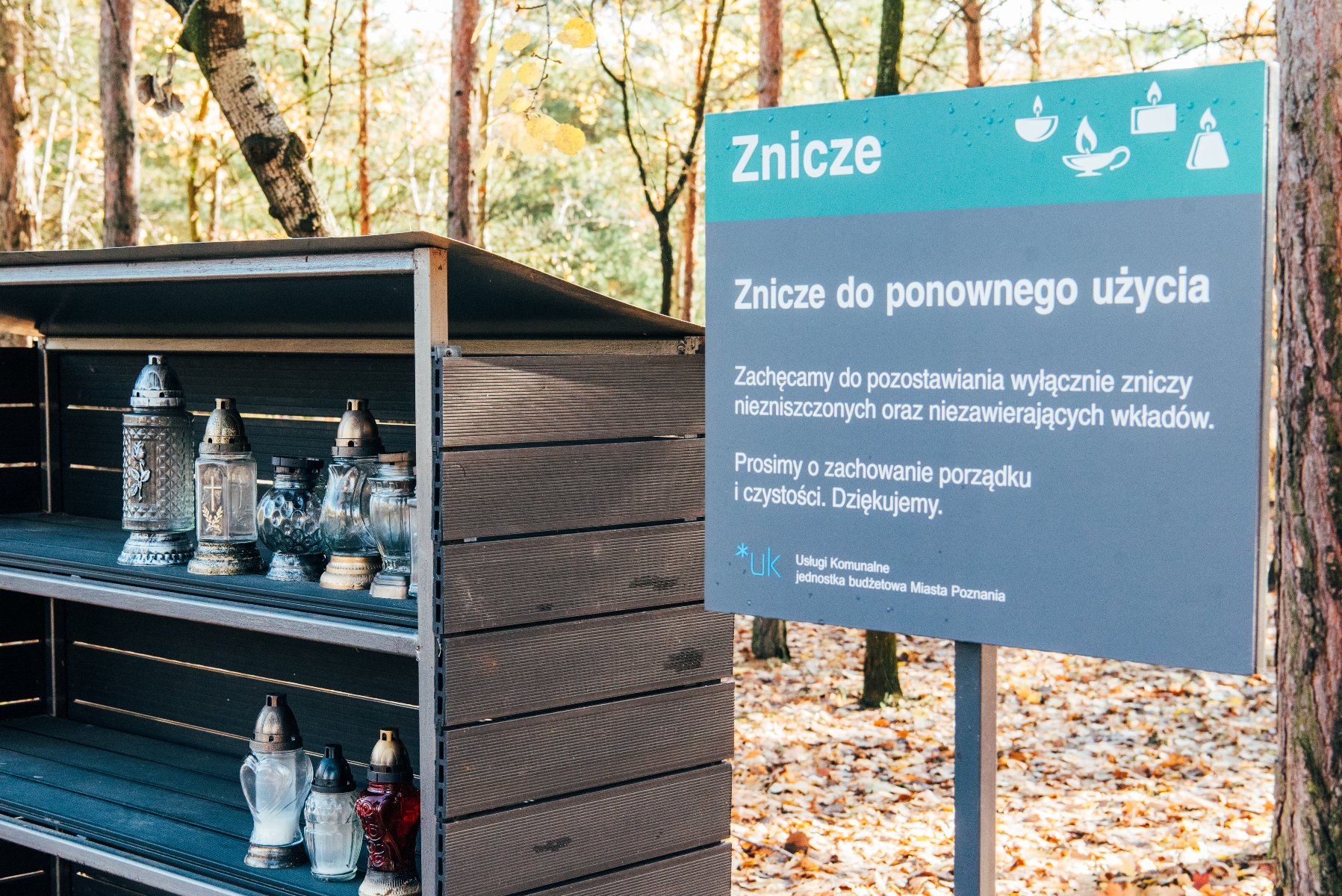 Zdjęcie przedstawia półkę ze zniczami oraz tablice informacyjną. - grafika rozmowy