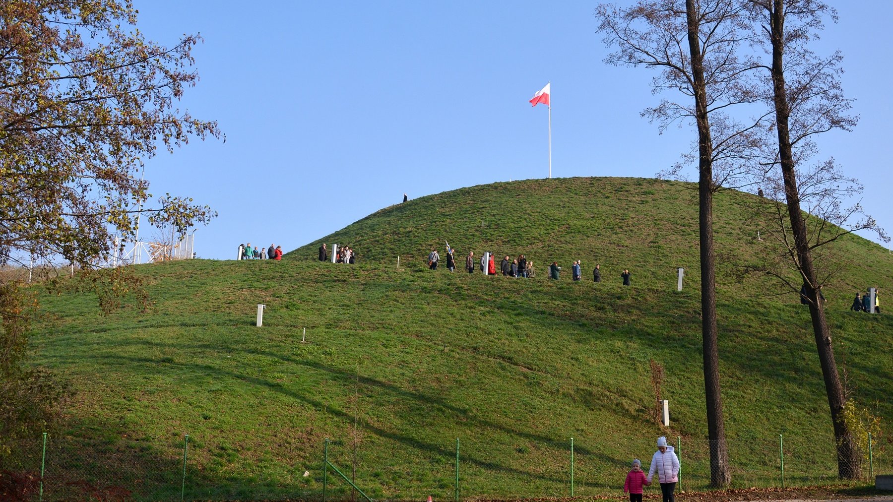 Zdjęcie przedstawia Kopiec Wolności i zwiedzajacych go ludzi. - grafika rozmowy