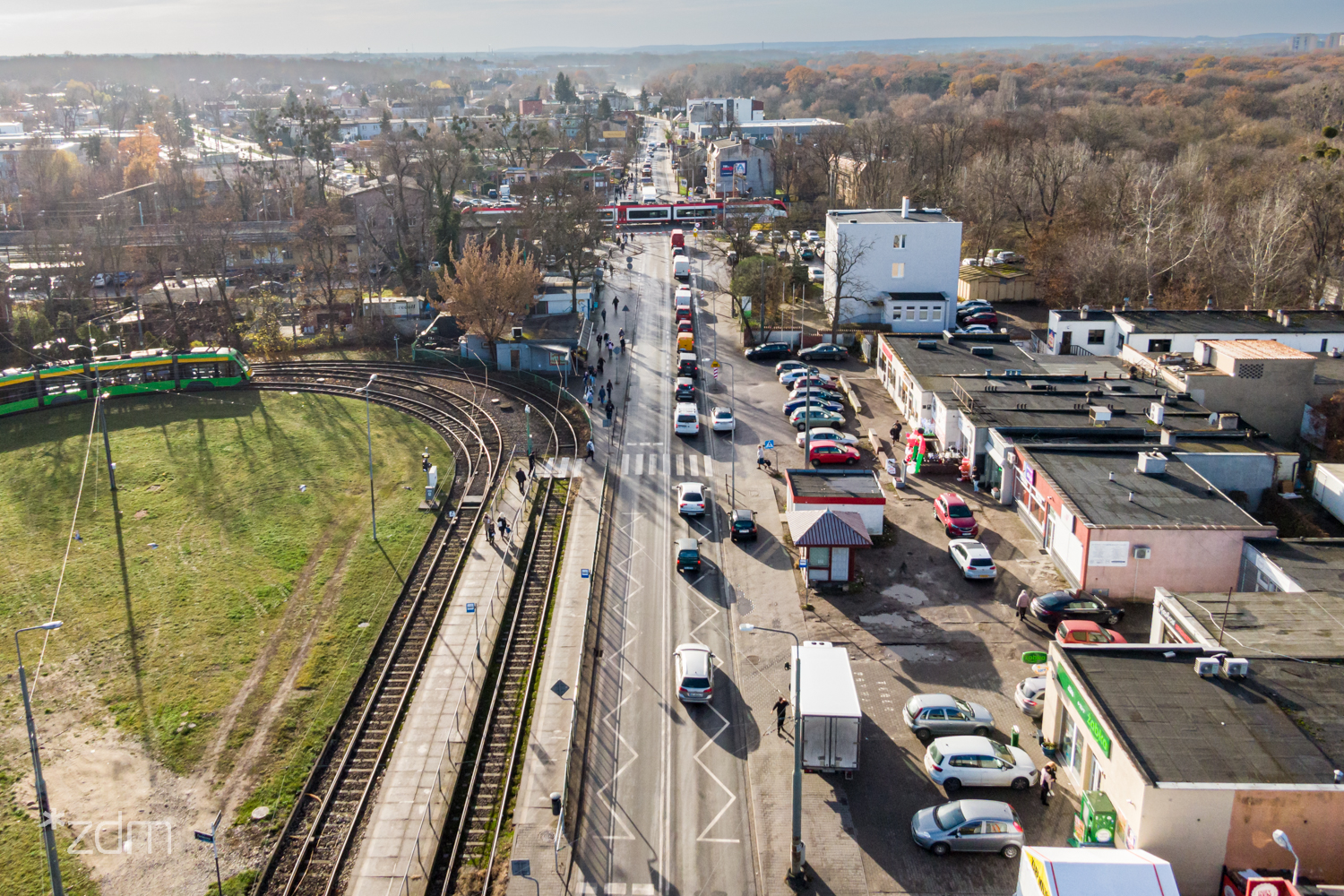 Widok z lotu ptaka na zamknięty przejazd kolejowy przy ul. Starołęckiej, przez który przejeżdża pociąg. Samochody czekają na otwracie szlabanów. Po prawej stronie jest pętla tramwajowa - grafika rozmowy