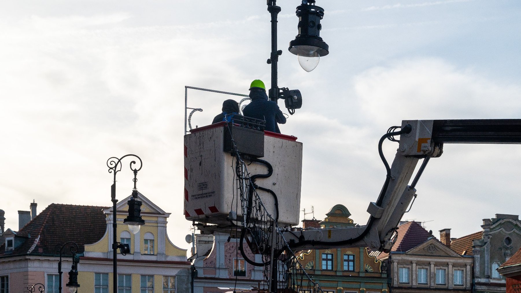 Zdjęcie przedstawia dwóch mężczyzn z wysięgniku podczas montażu iluminacji.