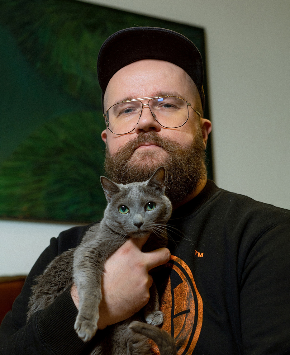 męzczyzna w czapce z daszkiem, okularach i brodą trzyma kota - grafika rozmowy