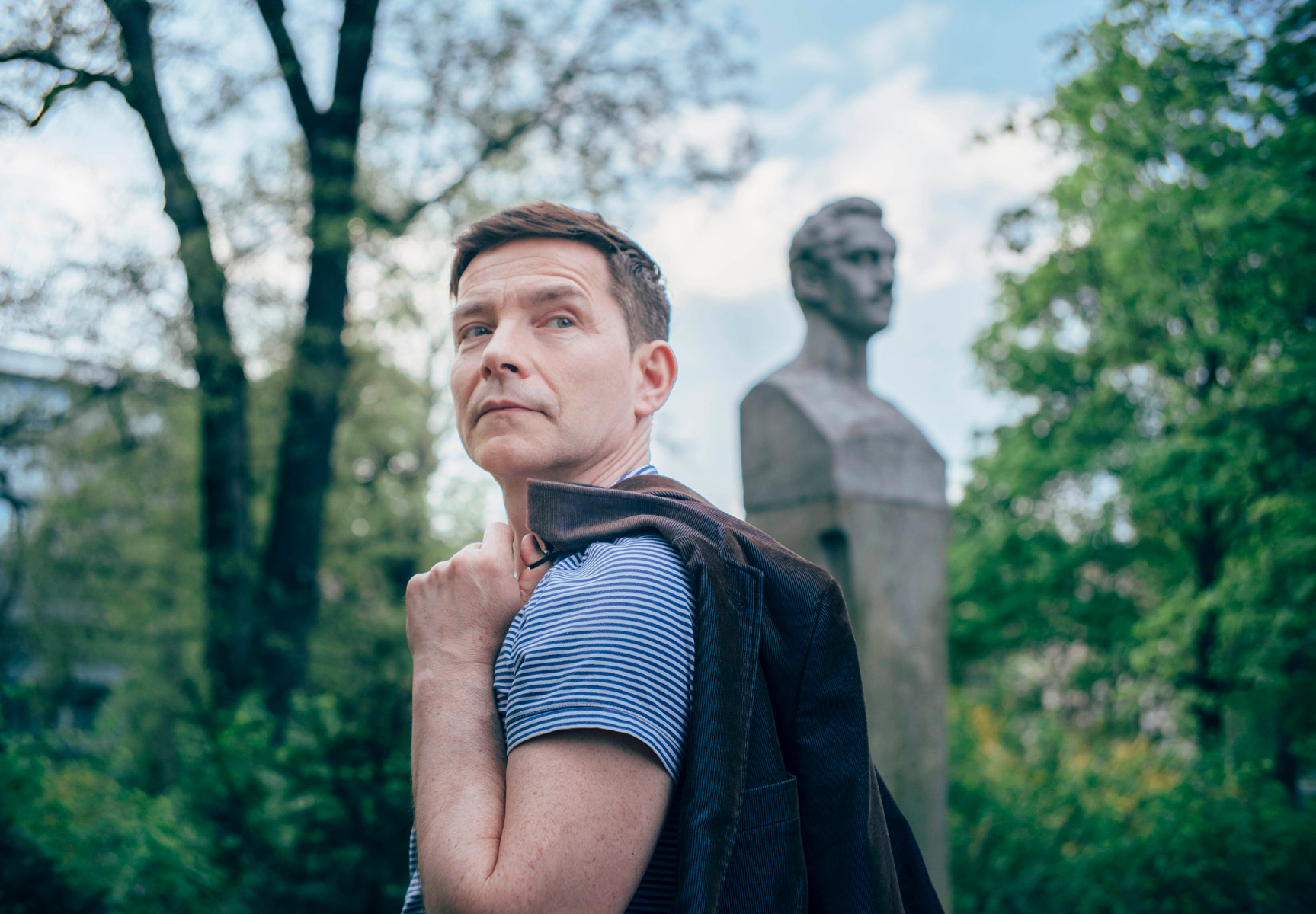 Mężczyzna z przewieszoną przez ramię marynarką stoi bokiem, patrzy w prawą stronę. - grafika rozmowy