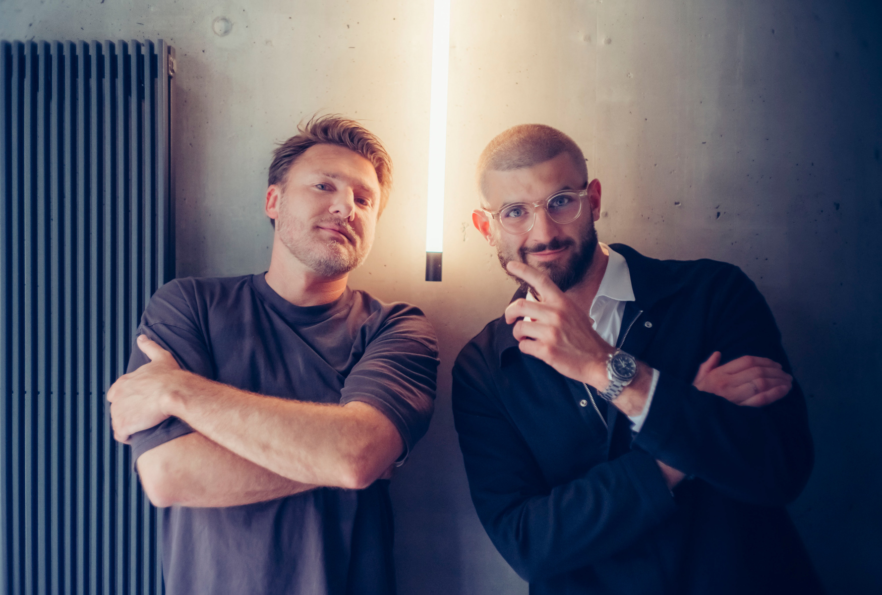 Dwóch młodych mężczyzn w krótkich włosach uśmiecha się w stronę obiektywu, jeden unosi palec wskazujący w stronę drugiego. - grafika rozmowy