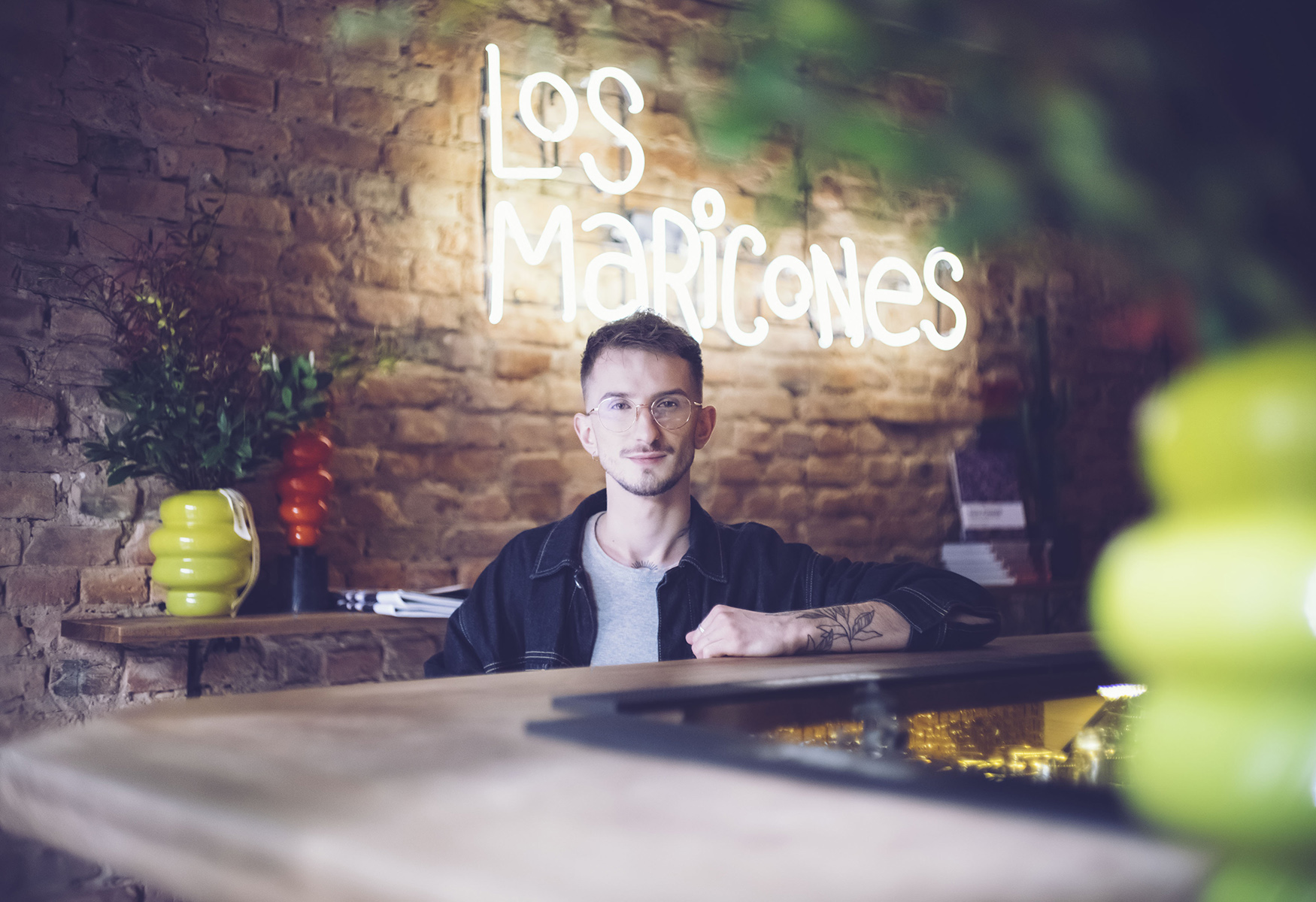 młody mężczyzna w okularach na tle ściany z neonowym napisem - grafika rozmowy