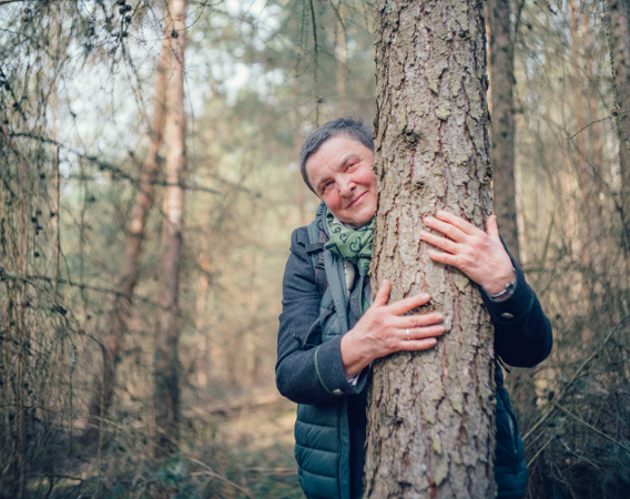 a woman with short hair hugs a tree in the forest