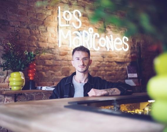 młody mężczyzna w okularach na tle ściany z neonowym napisem