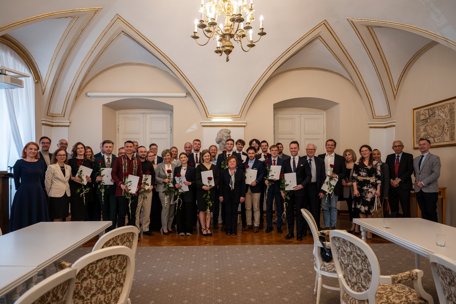 Zdjęcie przedstawia dwóch mężczyzn - młodszego i starszego - pozyjących do zdjęcia. Młodszy z nich trzyma w ręku teczkę.