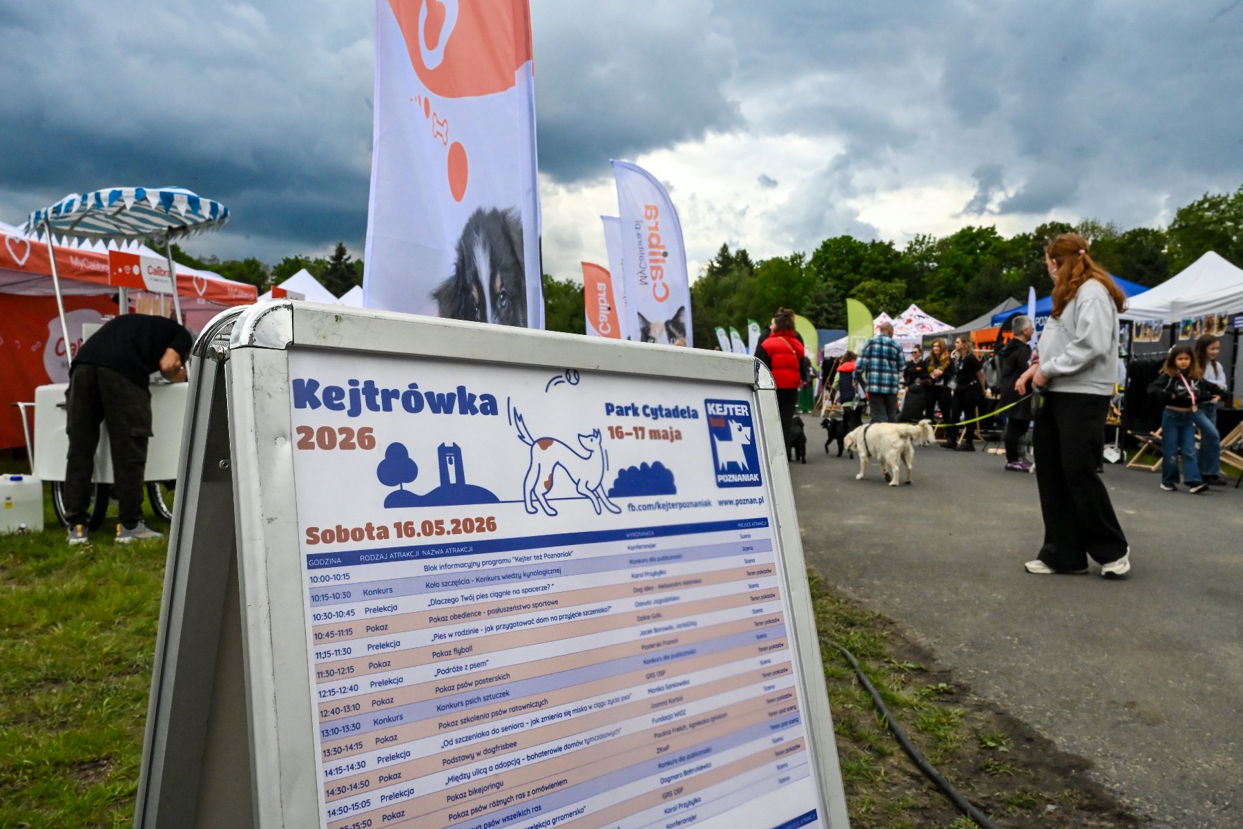 Zdjęcie przedstawia psa siedzącego na podwyższeniu i stojących wokół niego ludzi.